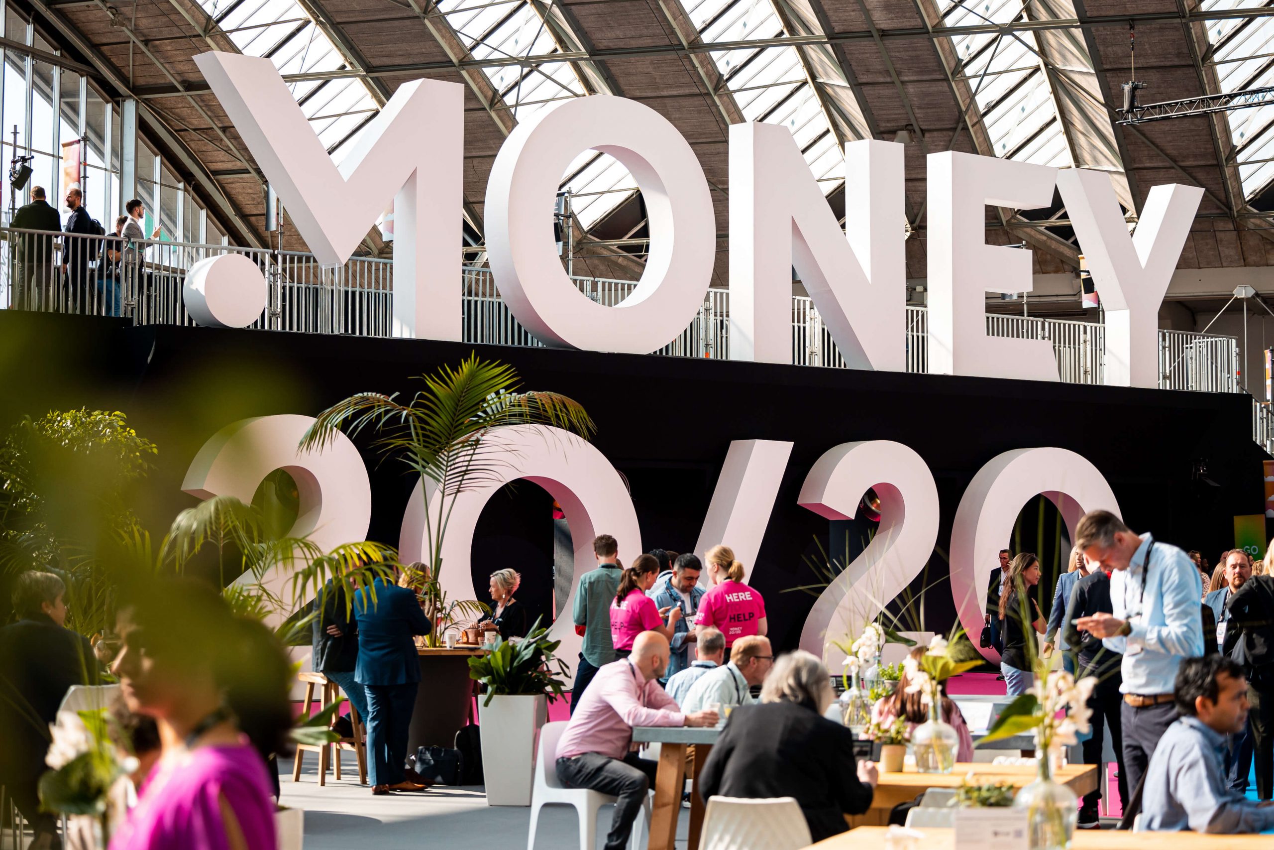A photograph of the large Money 20/20 sign, with chatting delegates surrounding it.