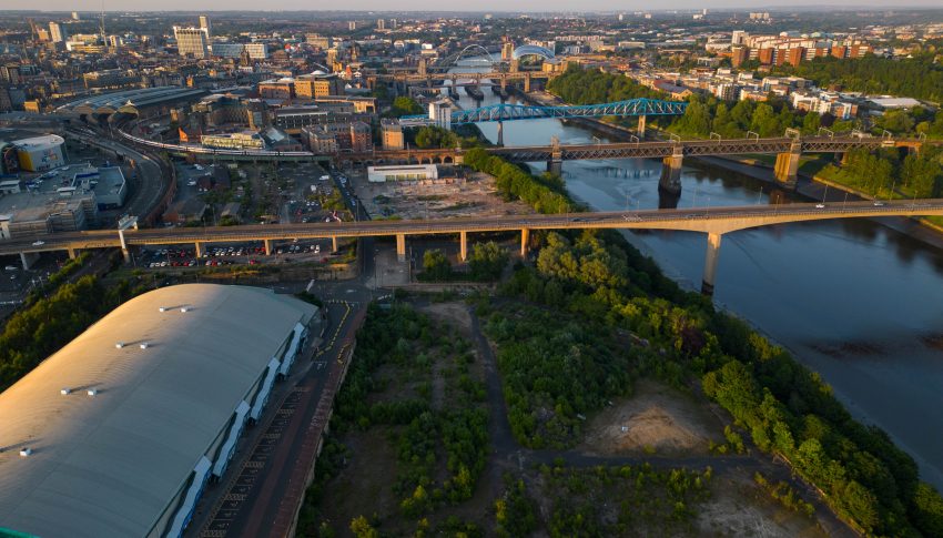 Aerial view of the Forth Yards site next to the River Tyne, there is a large arena to the bottom left and lots of brownfield across the rest of the site.