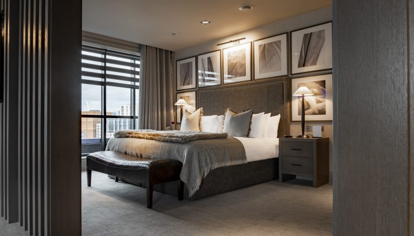 Grey and white themed hotel room with large double bed framed by large square photo frames and window to the left of the bed,